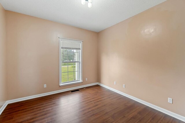 unfurnished room featuring dark wood-type flooring, visible vents, a textured ceiling, and baseboards