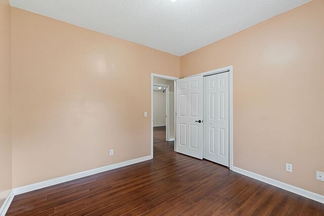 unfurnished bedroom featuring dark wood-style floors, a closet, and baseboards