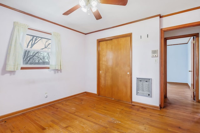 unfurnished bedroom featuring baseboards, light wood-style flooring, heating unit, crown molding, and a closet