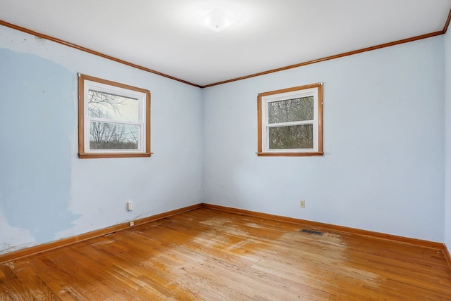 spare room featuring light wood-style floors, baseboards, visible vents, and ornamental molding