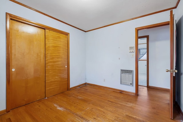 unfurnished bedroom with heating unit, light wood-style flooring, ornamental molding, and baseboards