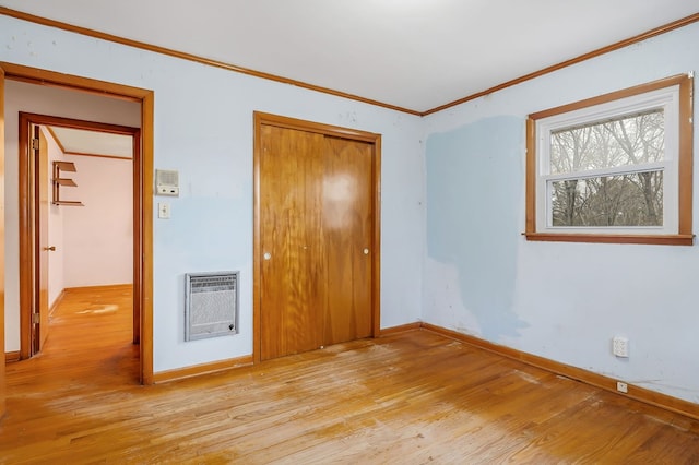 unfurnished bedroom with a closet, crown molding, heating unit, and wood finished floors