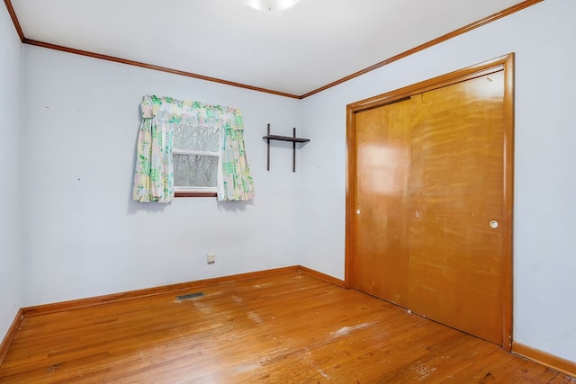 unfurnished bedroom featuring baseboards, visible vents, hardwood / wood-style floors, crown molding, and a closet