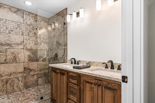 full bathroom with double vanity, a tile shower, and a sink