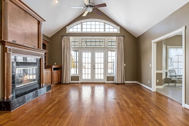 unfurnished living room with ceiling fan, french doors, wood finished floors, and a high end fireplace