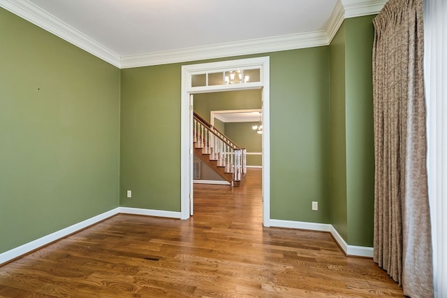 spare room with a chandelier, crown molding, baseboards, and wood finished floors