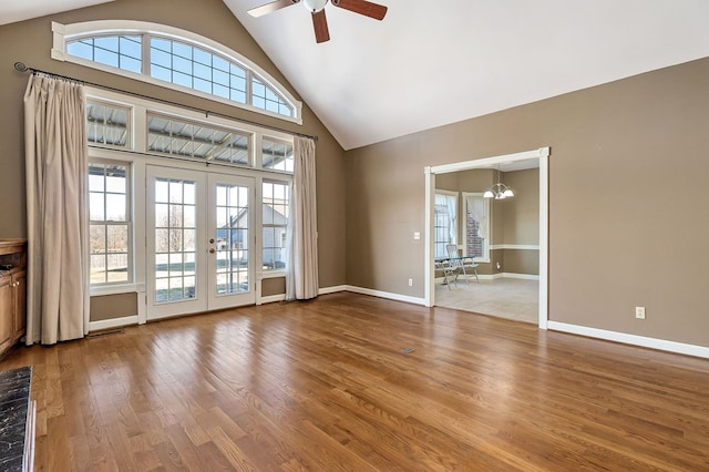 unfurnished living room featuring baseboards, wood finished floors, french doors, high vaulted ceiling, and ceiling fan with notable chandelier