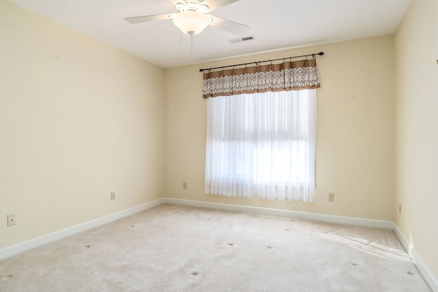 spare room with light colored carpet, visible vents, ceiling fan, and baseboards