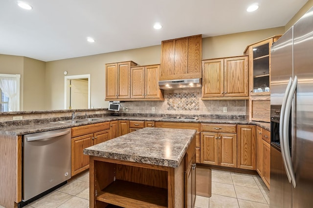 kitchen featuring appliances with stainless steel finishes, glass insert cabinets, a kitchen island, a sink, and under cabinet range hood