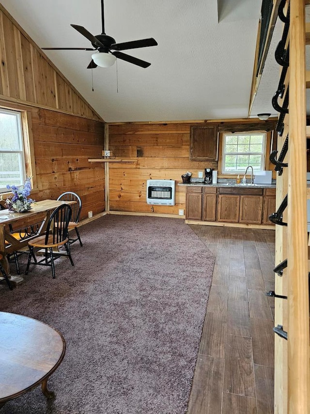 living room featuring dark wood-style flooring, heating unit, lofted ceiling, a ceiling fan, and wooden walls