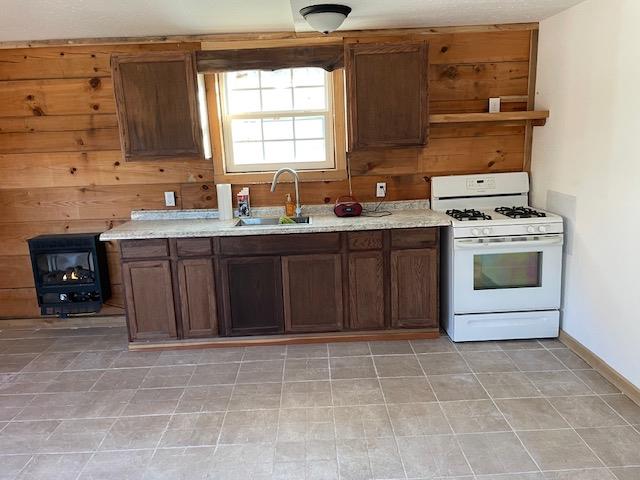 kitchen featuring dark brown cabinetry, white gas range oven, light stone counters, wood walls, and a sink