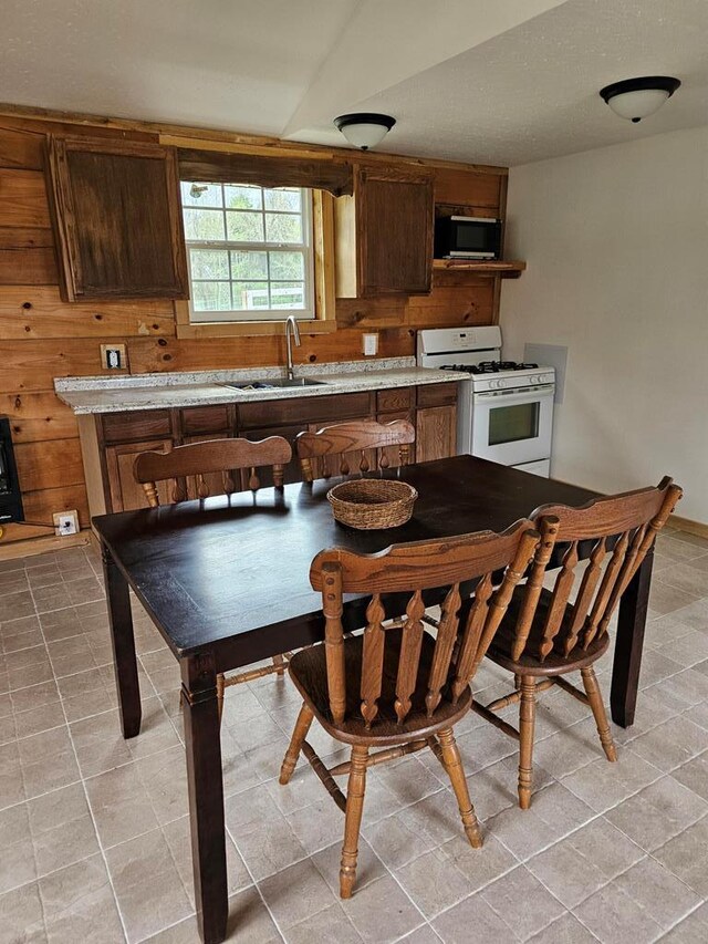 kitchen with brown cabinets, light tile patterned floors, white gas range, light countertops, and a sink