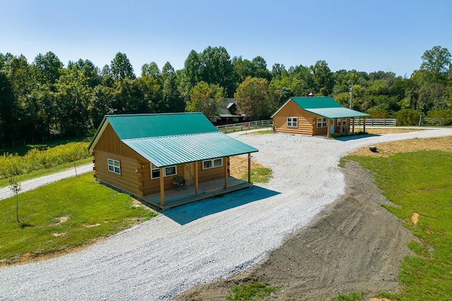 view of front of home featuring gravel driveway, a porch, a view of trees, log siding, and a front lawn