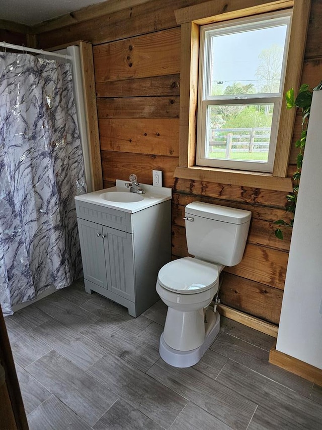 bathroom with toilet, curtained shower, wood walls, and vanity