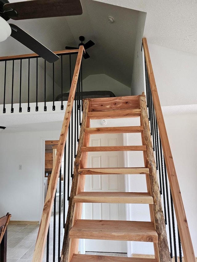 stairway featuring vaulted ceiling, a textured ceiling, and a ceiling fan