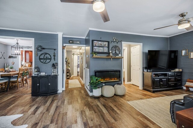 living area featuring ornamental molding, a glass covered fireplace, ceiling fan, and wood finished floors