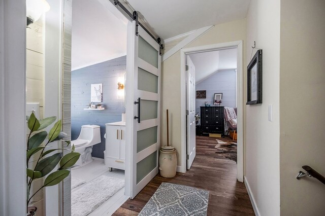 hallway featuring a barn door, wooden walls, and dark wood-type flooring