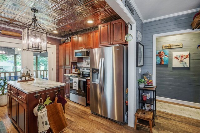 kitchen featuring an ornate ceiling, decorative light fixtures, appliances with stainless steel finishes, light wood-style floors, and a kitchen island