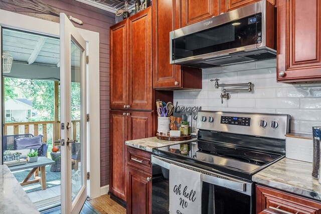 kitchen with light wood-style floors, appliances with stainless steel finishes, backsplash, and light stone counters