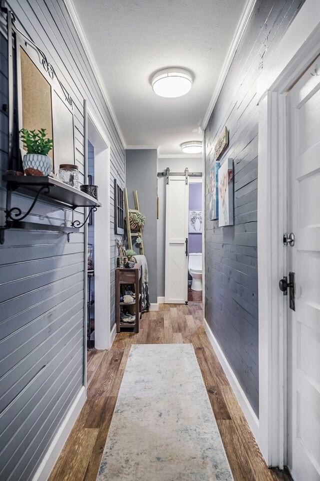 corridor with wood walls, a barn door, ornamental molding, and wood finished floors