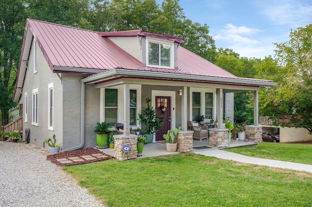 view of front facade with metal roof, a porch, a front yard, and stucco siding