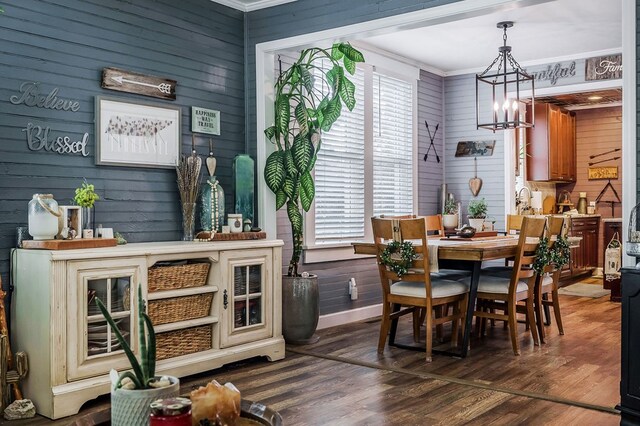 dining space featuring dark wood-style floors, ornamental molding, wood walls, and an inviting chandelier