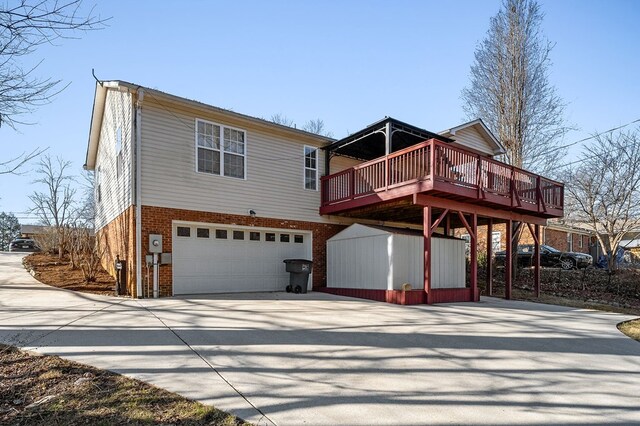 rear view of house featuring an attached garage, a deck, concrete driveway, and brick siding