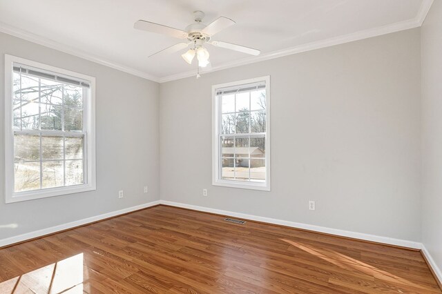 empty room featuring baseboards, crown molding, visible vents, and wood finished floors