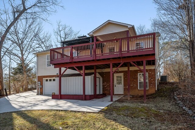 rear view of house with a garage, driveway, brick siding, and a wooden deck