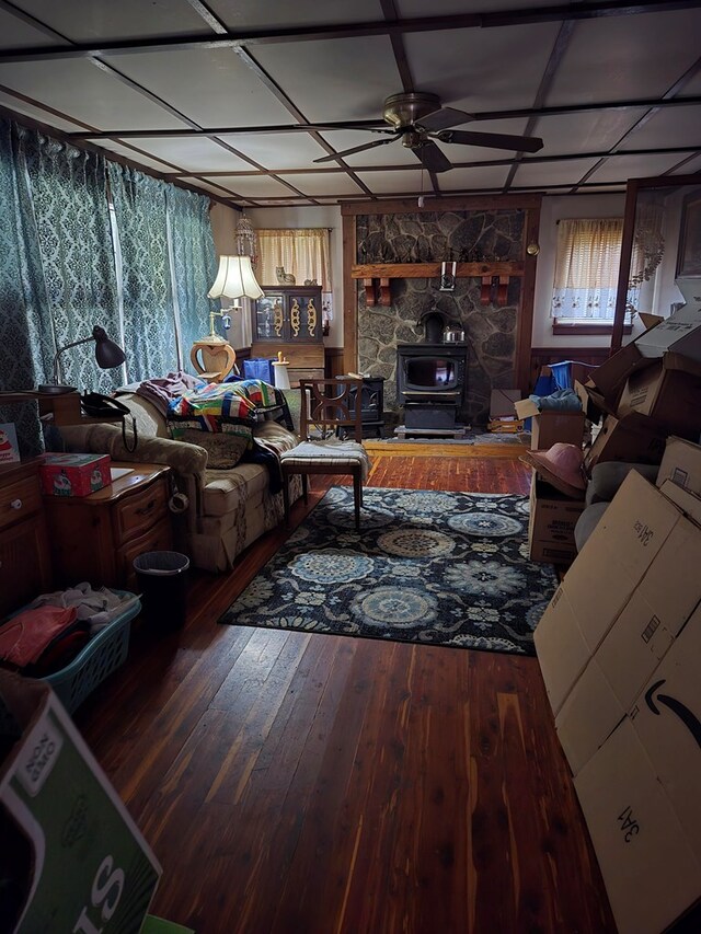 living area featuring a ceiling fan, a wood stove, and wood finished floors