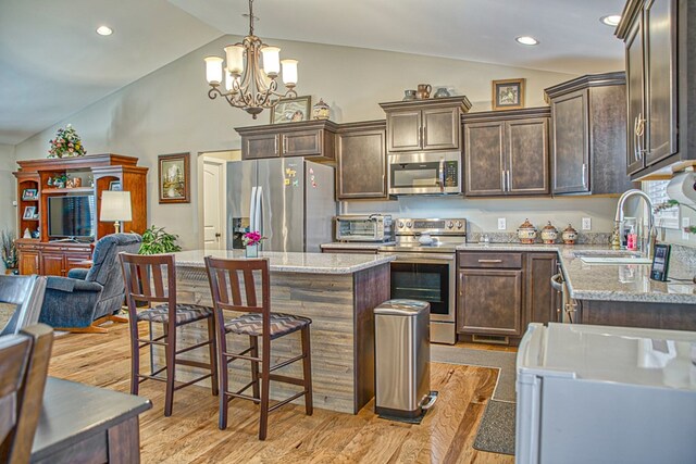 kitchen with a kitchen island, appliances with stainless steel finishes, open floor plan, light stone countertops, and a sink