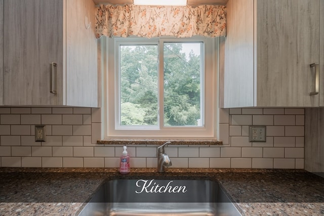 kitchen with light brown cabinetry, dark stone countertops, a sink, and decorative backsplash