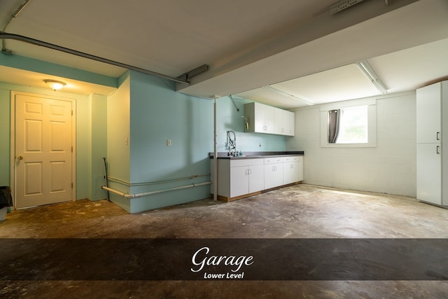 kitchen featuring dark countertops, white cabinetry, concrete floors, and concrete block wall