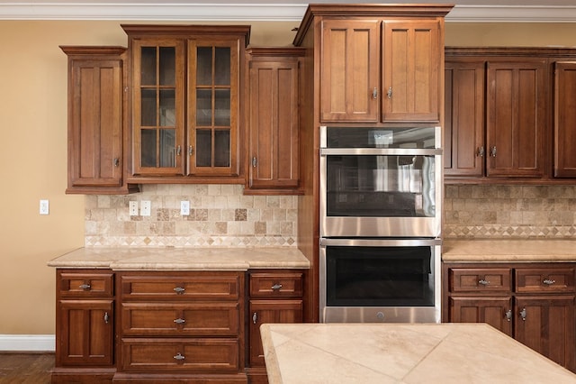 kitchen with glass insert cabinets, stainless steel double oven, light countertops, and backsplash