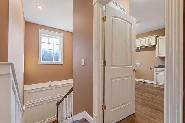 corridor with dark wood-style flooring, a wainscoted wall, a decorative wall, and an upstairs landing