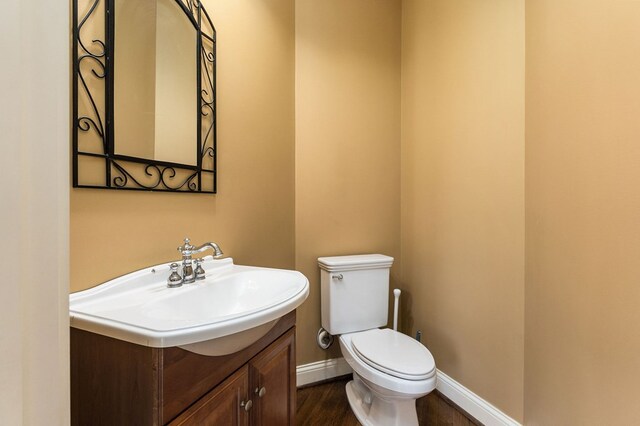 half bathroom with toilet, baseboards, wood finished floors, and vanity