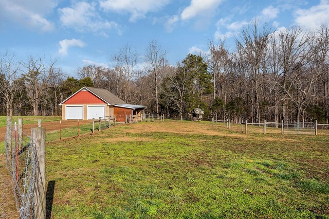 view of yard featuring driveway, a rural view, fence, and an outdoor structure