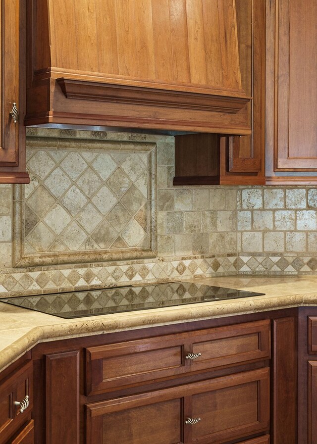 kitchen featuring light countertops, backsplash, custom exhaust hood, and black electric cooktop