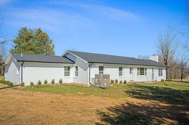 back of house with brick siding, a lawn, cooling unit, and a chimney