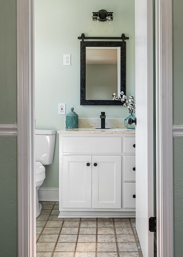 half bath with stone tile floors, toilet, vanity, and baseboards