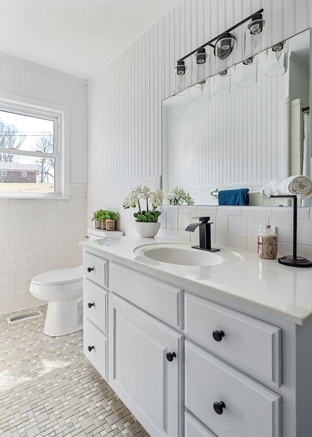 bathroom featuring visible vents, toilet, vanity, ornamental molding, and tile walls