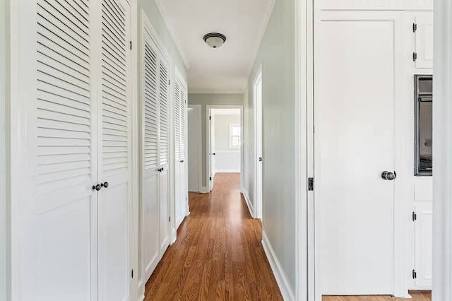 corridor featuring crown molding, baseboards, and wood finished floors