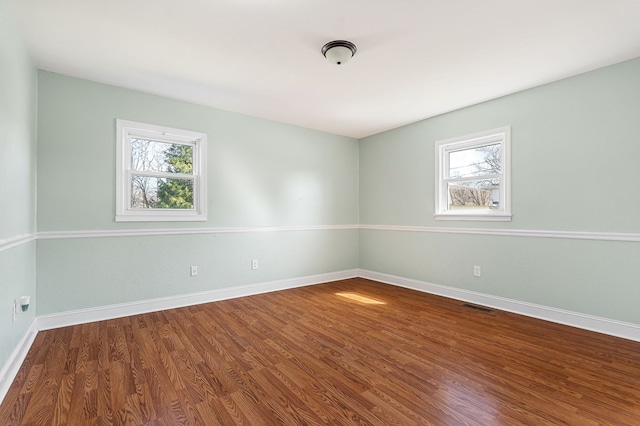 unfurnished room featuring a wealth of natural light, visible vents, baseboards, and wood finished floors