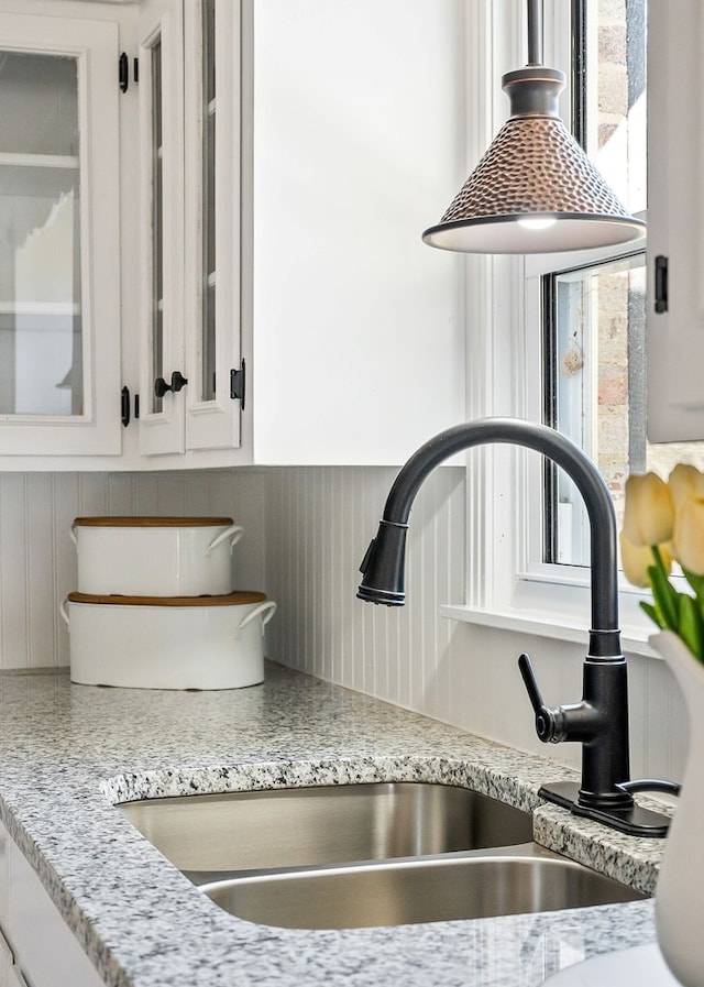 interior details with tasteful backsplash, glass insert cabinets, light stone countertops, white cabinetry, and a sink