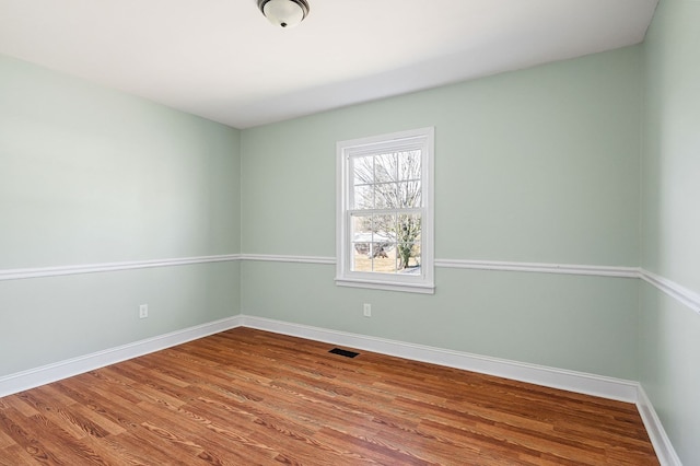 unfurnished room with wood finished floors, visible vents, and baseboards