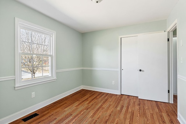 unfurnished bedroom with visible vents, baseboards, a closet, and wood finished floors