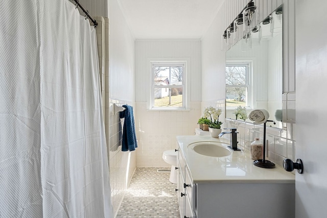 bathroom with a wainscoted wall, toilet, tile walls, tile patterned flooring, and vanity