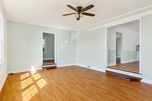 empty room featuring crown molding, light wood-type flooring, and baseboards