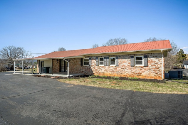 ranch-style house featuring metal roof, a carport, central AC, and brick siding