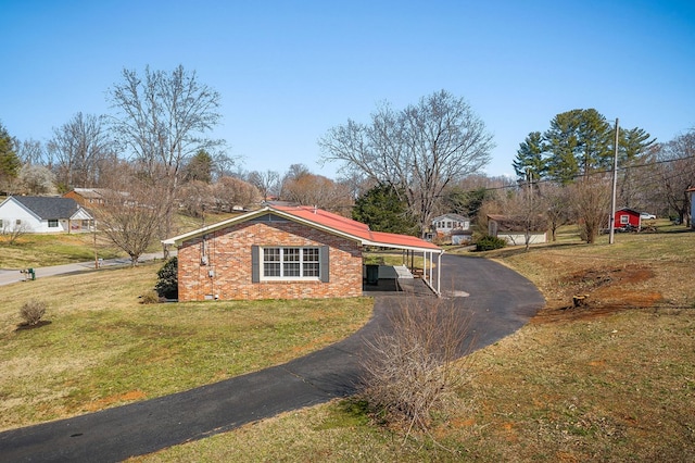 view of side of property with brick siding, an attached carport, aphalt driveway, a lawn, and crawl space